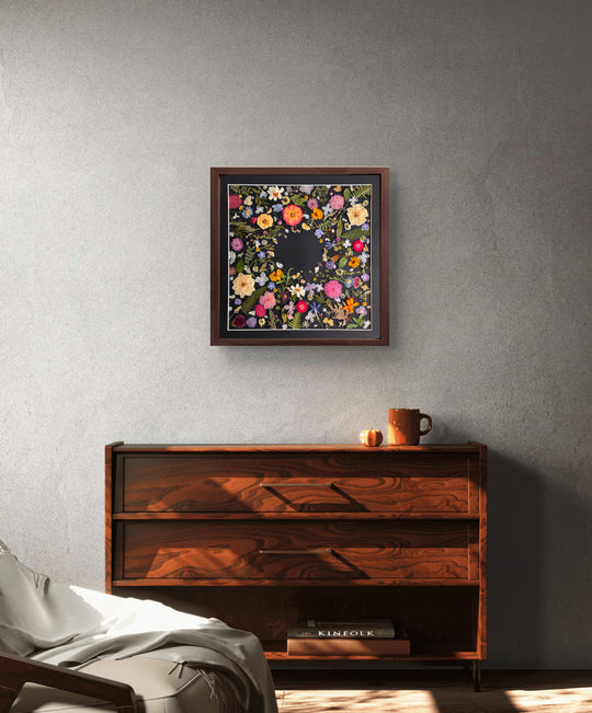 black background pressed flower frame art with flower petals hanging on the living room wall above wood desk
