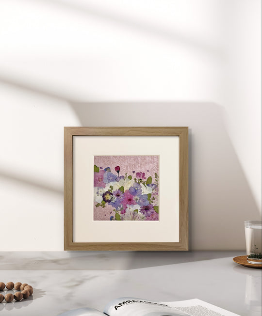 10 inches width 10 inches height pressed flower frame art that has pink theme stands on the table.