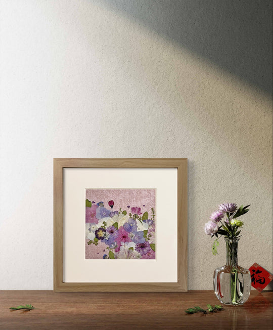 10 inches width 10 inches height pressed flower frame art that has pink theme stands on the wood table.