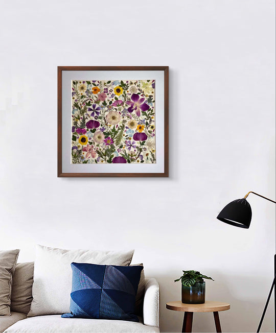 15.7 inch width 15.7 inch height pressed flower frame art that has vibrant and colorful petals formed design hanging on the white wall above couch.